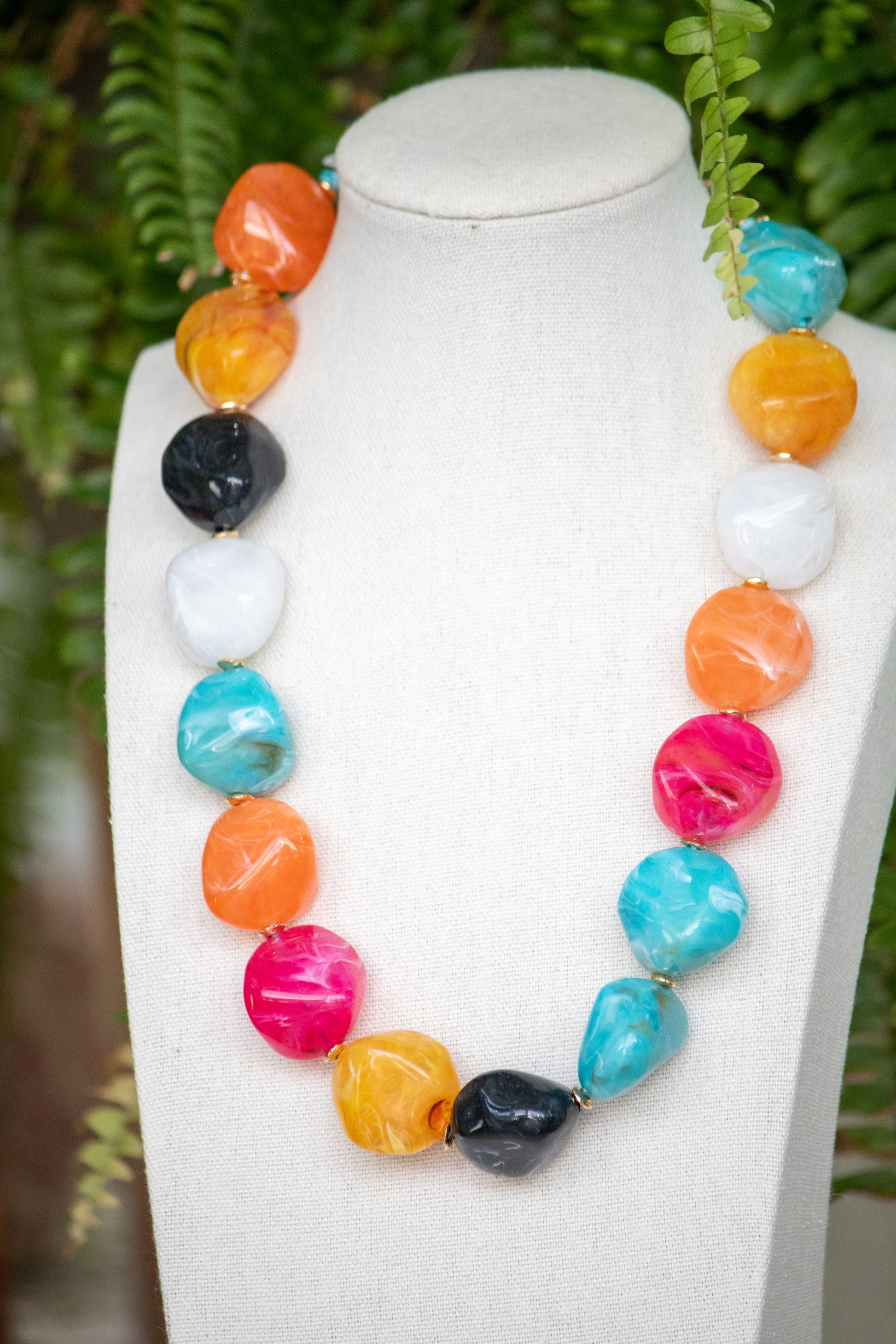 Colorful beaded necklace on a mannequin against a green leafy background