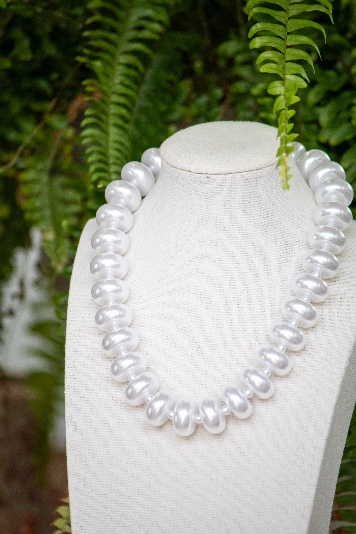 Pearl necklace on a mannequin with a green leafy background