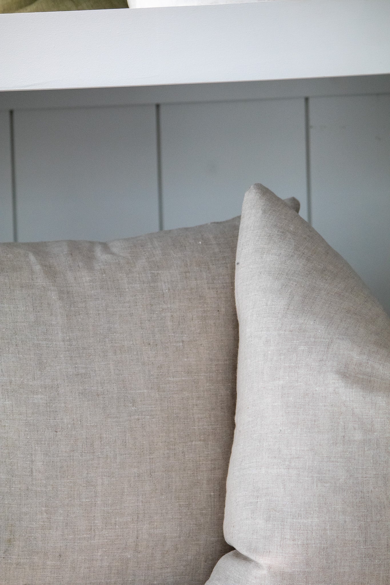 Two beige pillows on a white surface with a light gray wall in the background