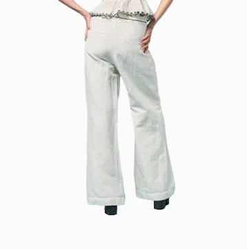 Woman wearing a white one-shoulder top and white pants against a light blue background