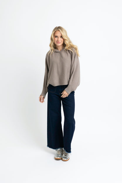 Woman wearing a gray sweater and dark jeans on a white background