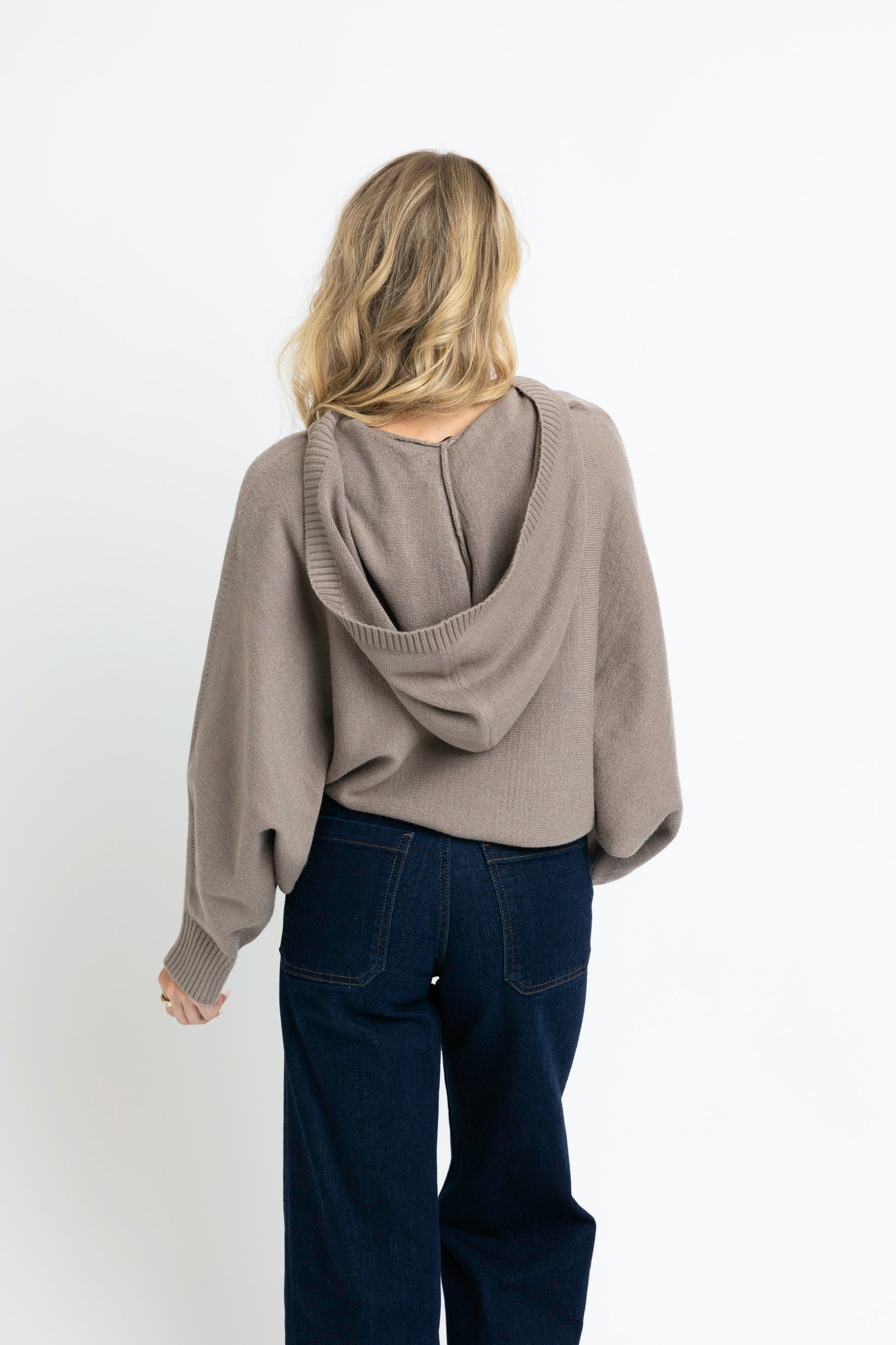 Person wearing a beige sweater with a hood on a white background