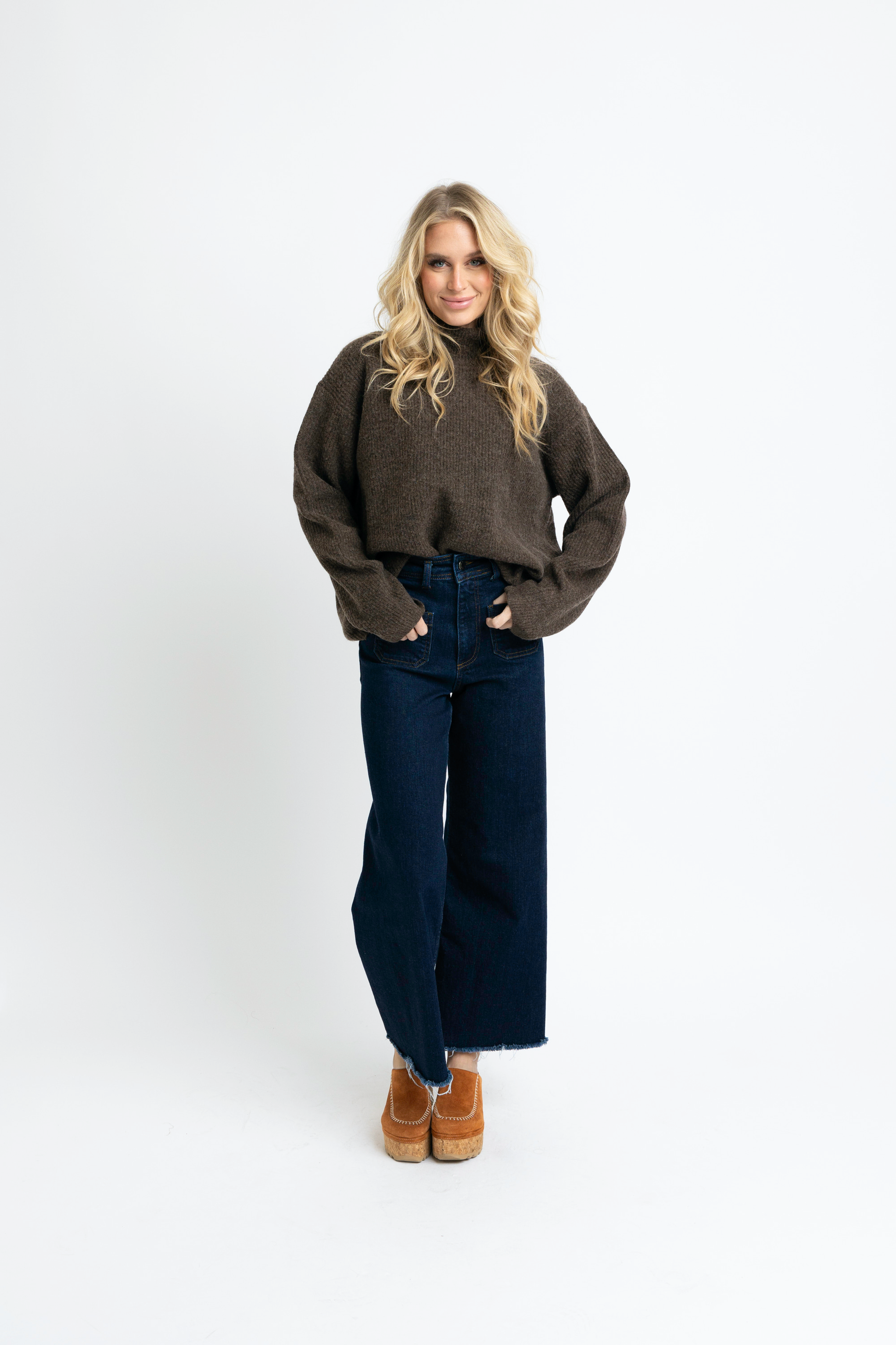 Woman wearing a brown sweater and dark blue jeans on a white background