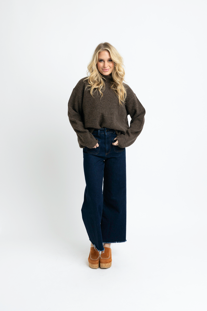 Woman wearing a brown sweater and dark blue jeans on a white background