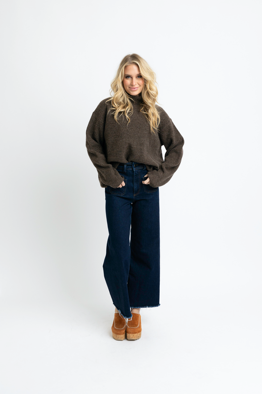 Woman wearing a brown sweater and dark blue jeans on a white background