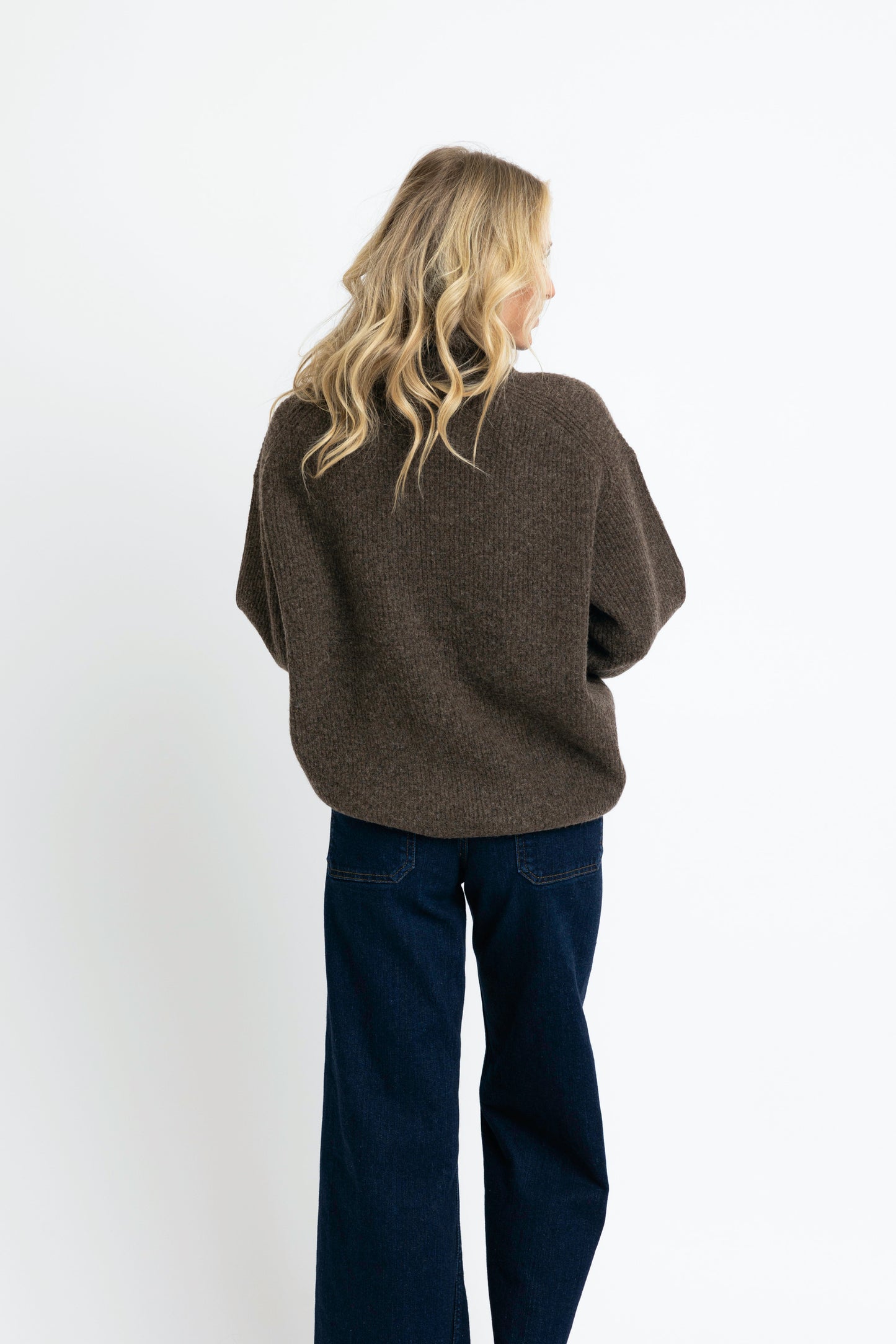 Person wearing a brown sweater and dark blue jeans on a white background