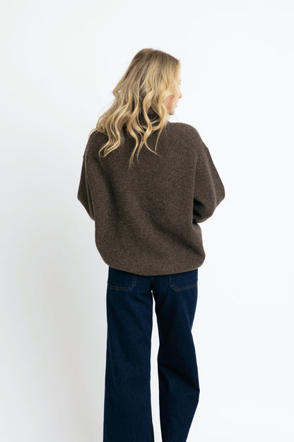 Person wearing a brown sweater and dark blue jeans on a white background