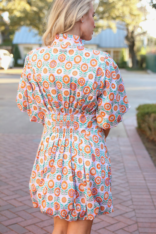 Woman wearing a floral dress walking outdoors on a sidewalk.