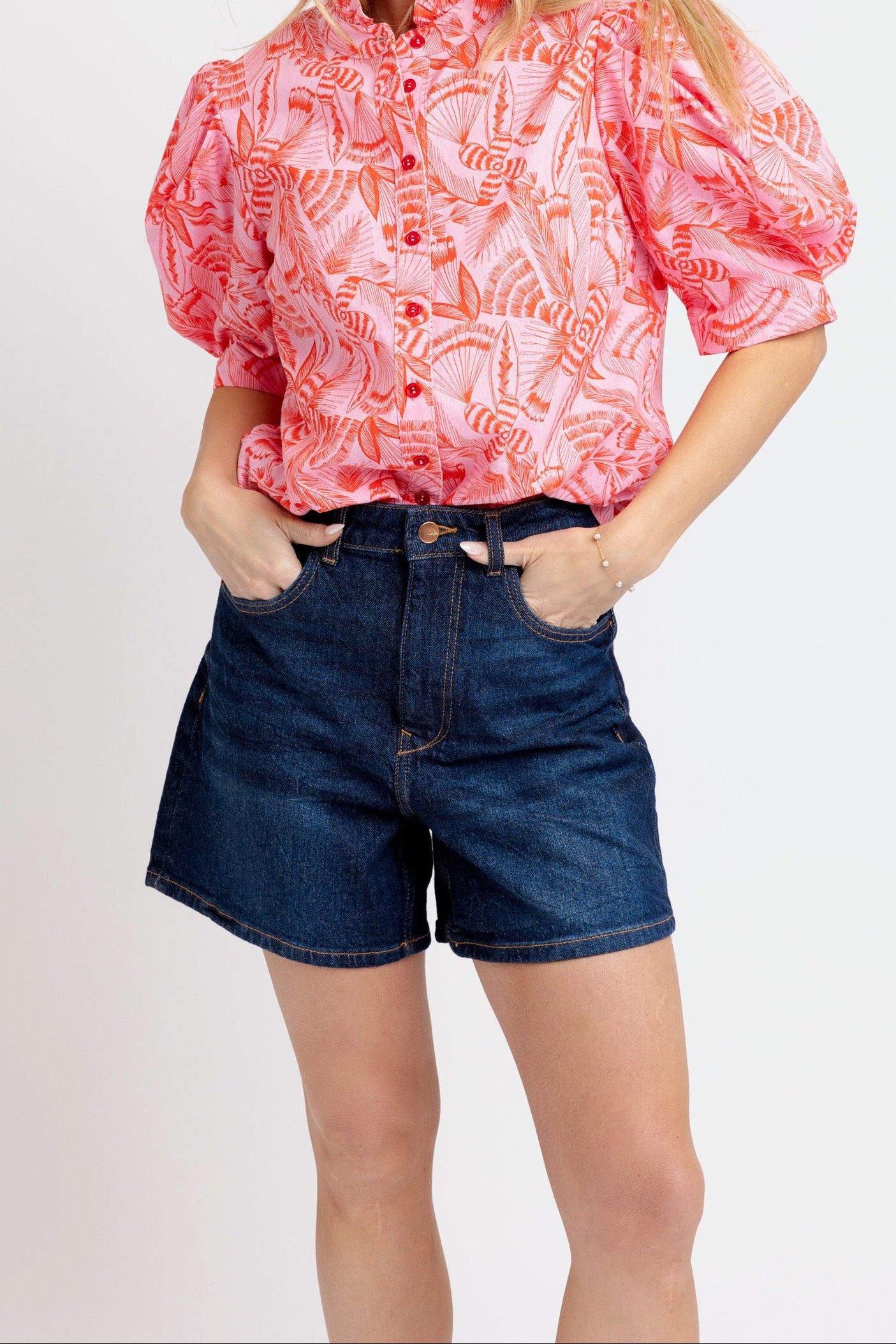 Woman wearing a pink patterned blouse and blue shorts on a white background