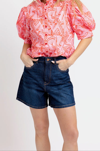 Woman wearing a pink patterned blouse and blue shorts on a white background