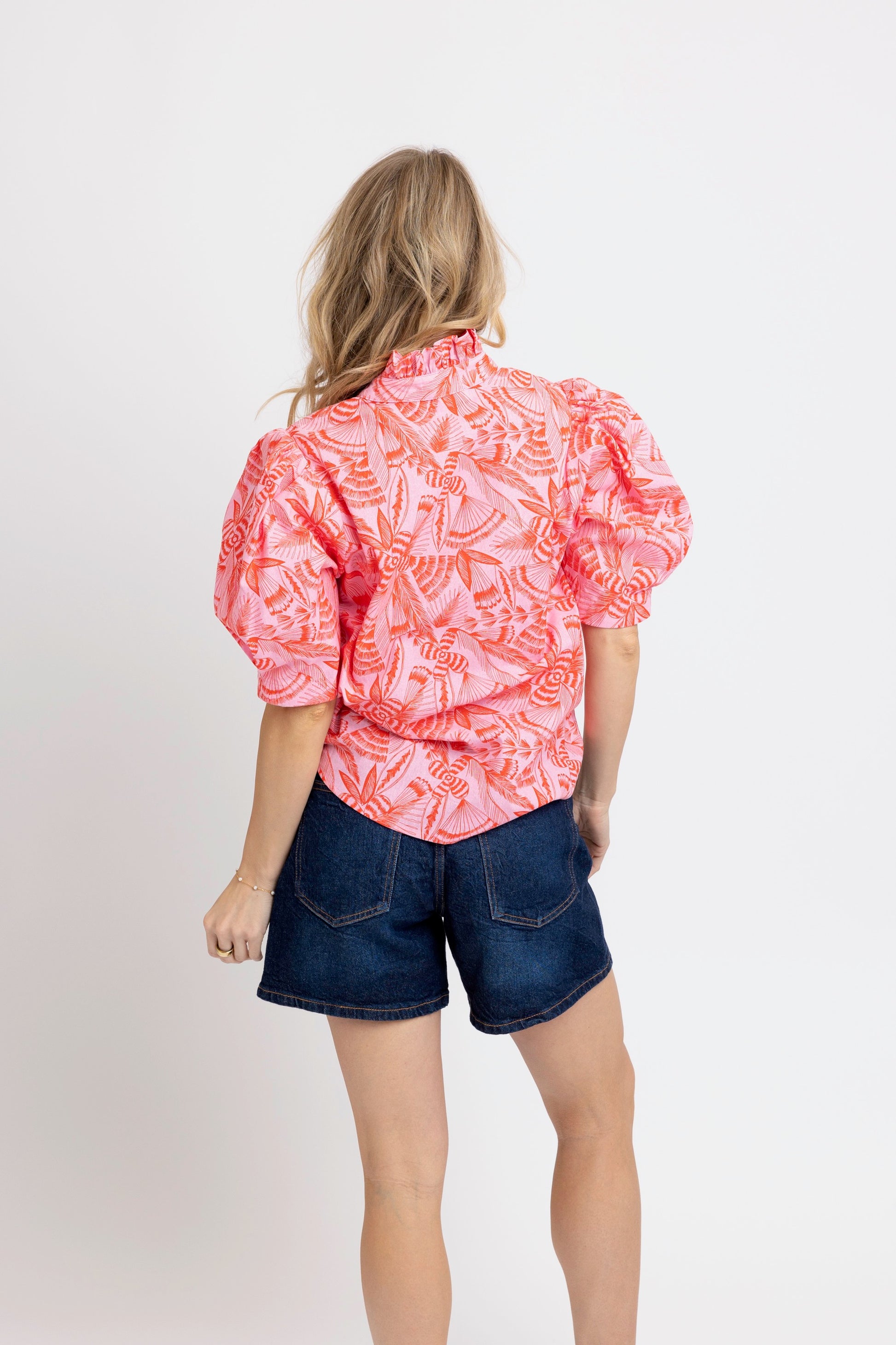 Person wearing a pink patterned blouse and blue shorts on a white background