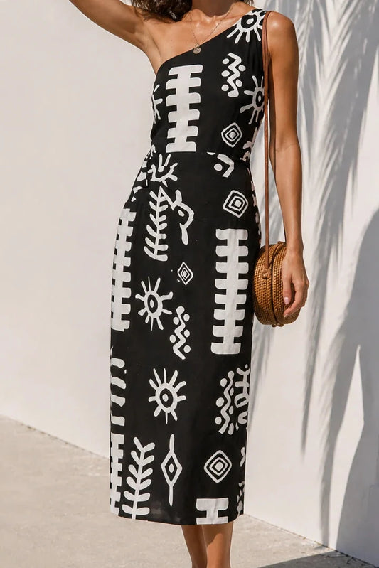 Woman wearing a black and white patterned dress against a white wall.