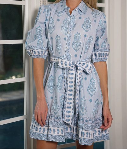 Woman wearing a light blue patterned dress standing indoors.