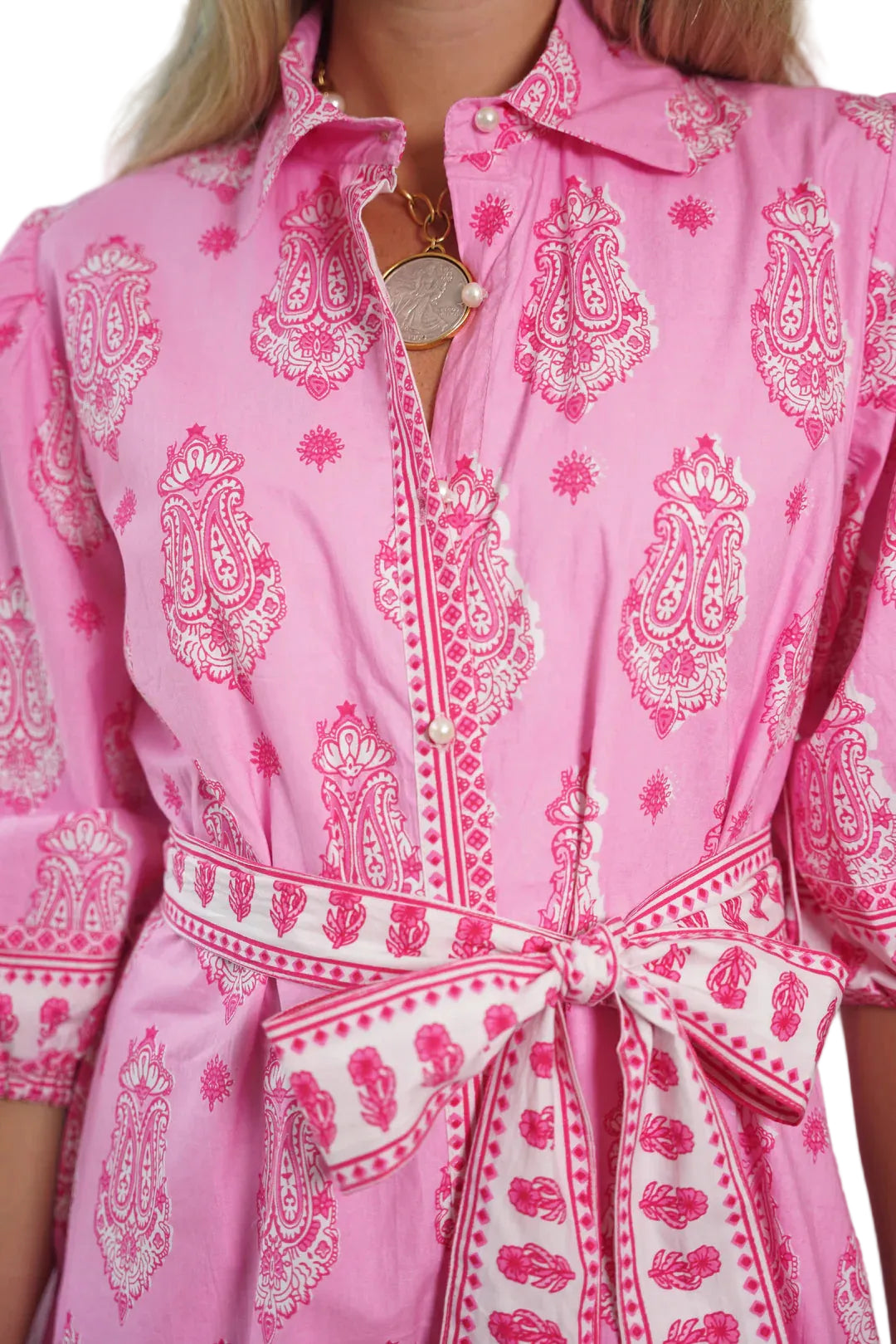Close-up of a pink dress with white paisley patterns and a belt.