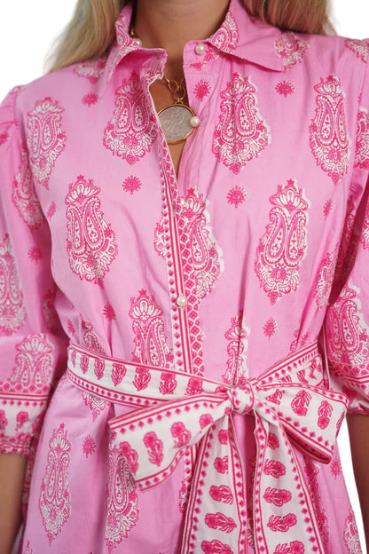 Close-up of a pink dress with white paisley patterns and a belt.