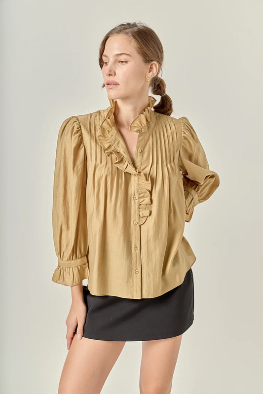 Woman wearing a beige blouse with ruffled details and a black skirt on a plain background