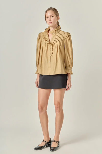 Woman wearing a beige blouse with ruffled details and a black skirt on a plain background