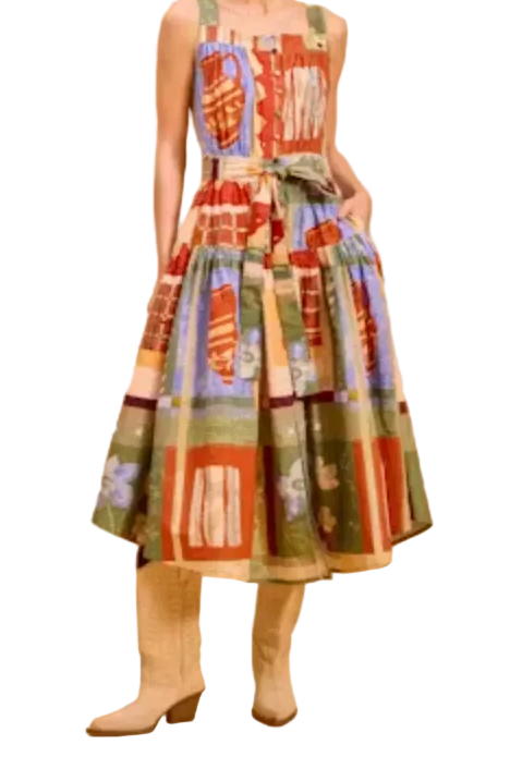 A woman modeling a sleeveless midi dress with a colorful patchwork print in red, green, blue, and beige tones, paired with beige ankle boots, against a solid warm beige studio background.