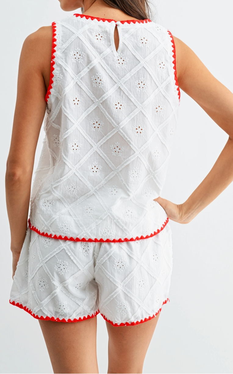 Woman wearing a white embroidered outfit with red trim on a plain background