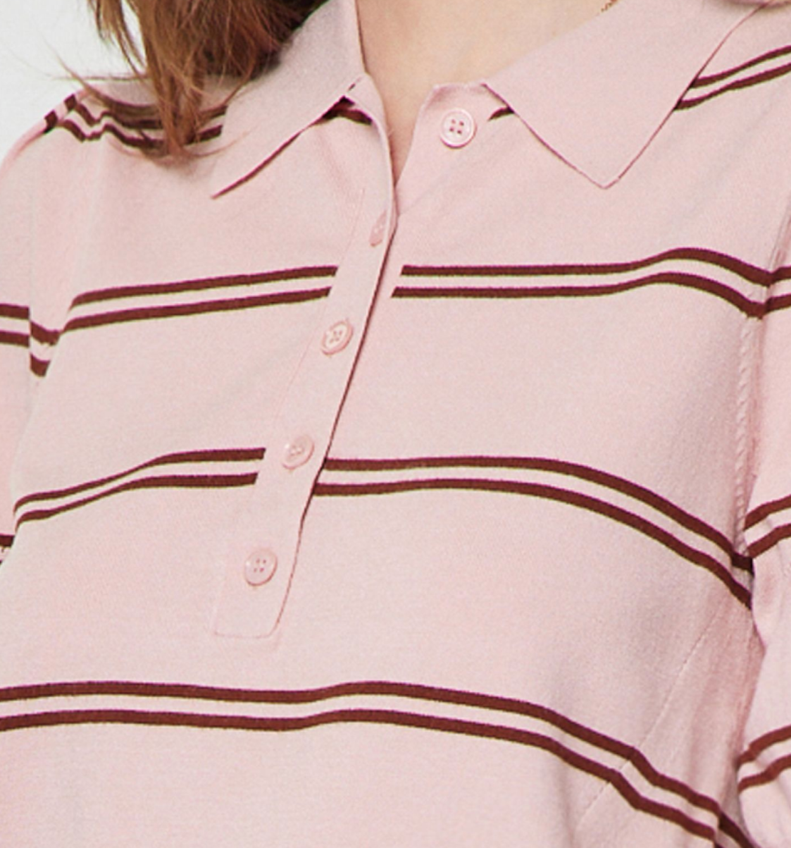 A close-up of a light pink knit polo shirt with dark brown horizontal stripes and a buttoned collar, worn by a model.