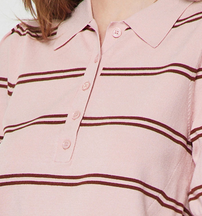 A close-up of a light pink knit polo shirt with dark brown horizontal stripes and a buttoned collar, worn by a model.