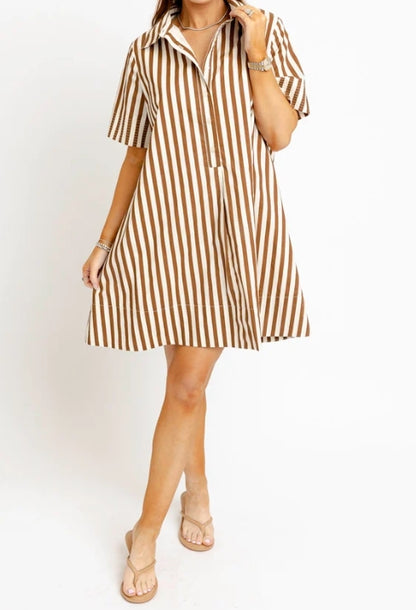 A woman modeling a short-sleeve collared shift dress with vertical brown and beige stripes, paired with beige flat sandals against a plain white studio background.