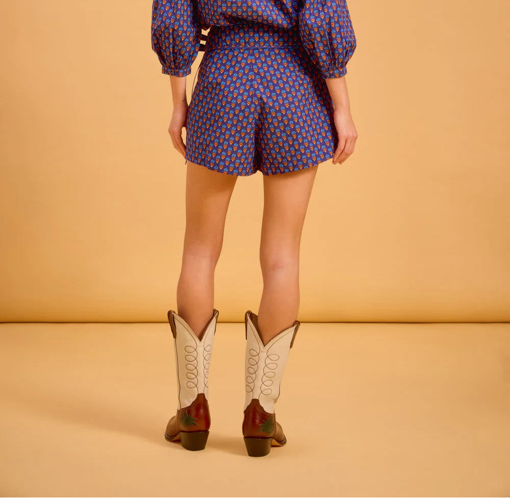 Person wearing a patterned outfit with cowboy boots on a beige background