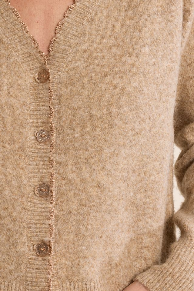 Close-up of a beige knit cardigan sweater with a V-neck, frayed trim, and brown buttons, worn by a model.