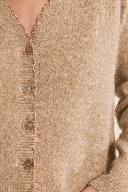 Close-up of a beige knit cardigan sweater with a V-neck, frayed trim, and brown buttons, worn by a model.