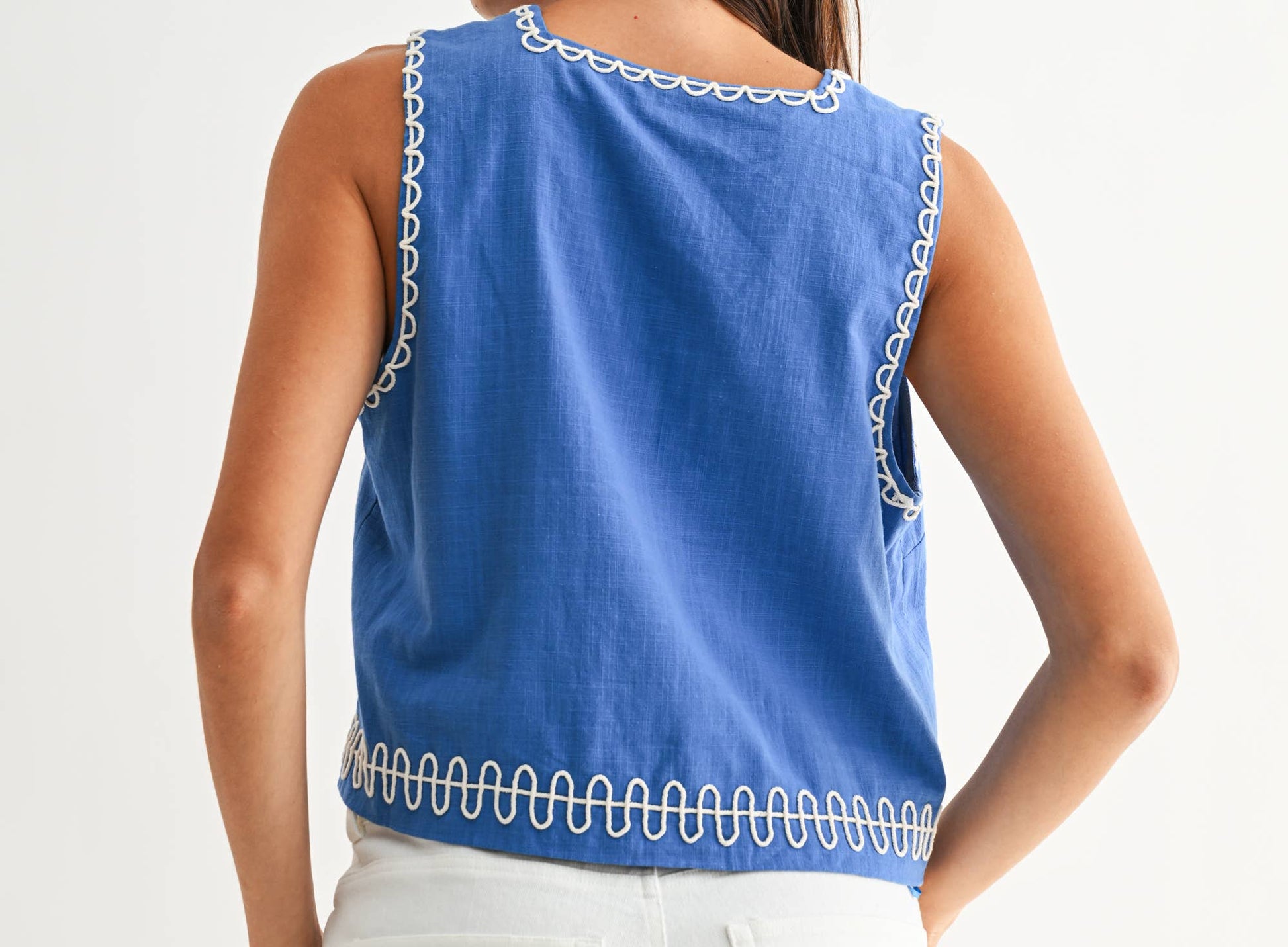 Woman wearing a blue sleeveless top with white trim on a white background