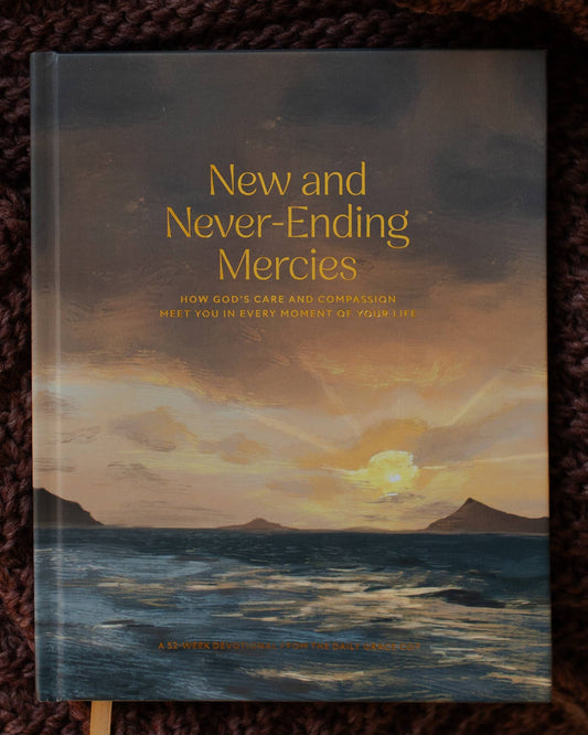 Book titled 'New and Never-Ending Mercies' with a sunset over water illustration, placed on a textured surface with a knitted brown blanket.