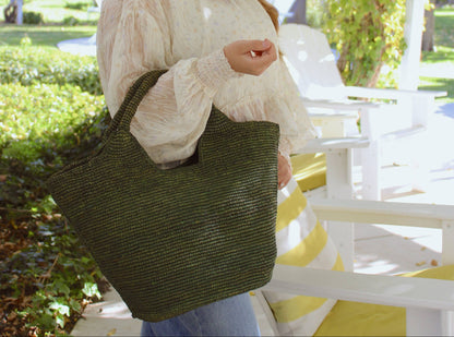 Woman wearing a colorful hat and holding a green bag in an outdoor setting