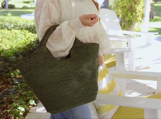 Woman wearing a colorful hat and holding a green bag in an outdoor setting