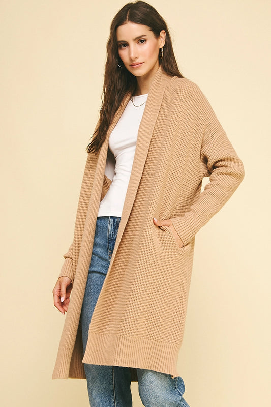 Woman wearing a beige cardigan over a white shirt and blue jeans on a beige background