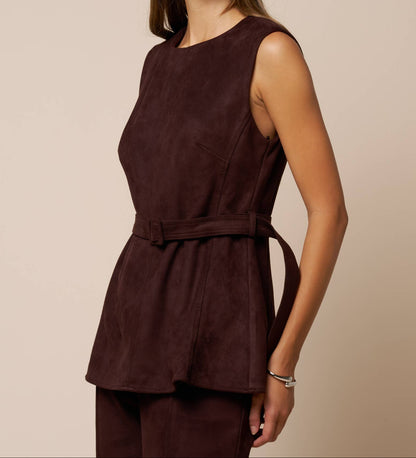 A woman modeling a sleeveless dark brown peplum top with a matching waist tie, paired with matching dark brown trousers, against a solid beige background.