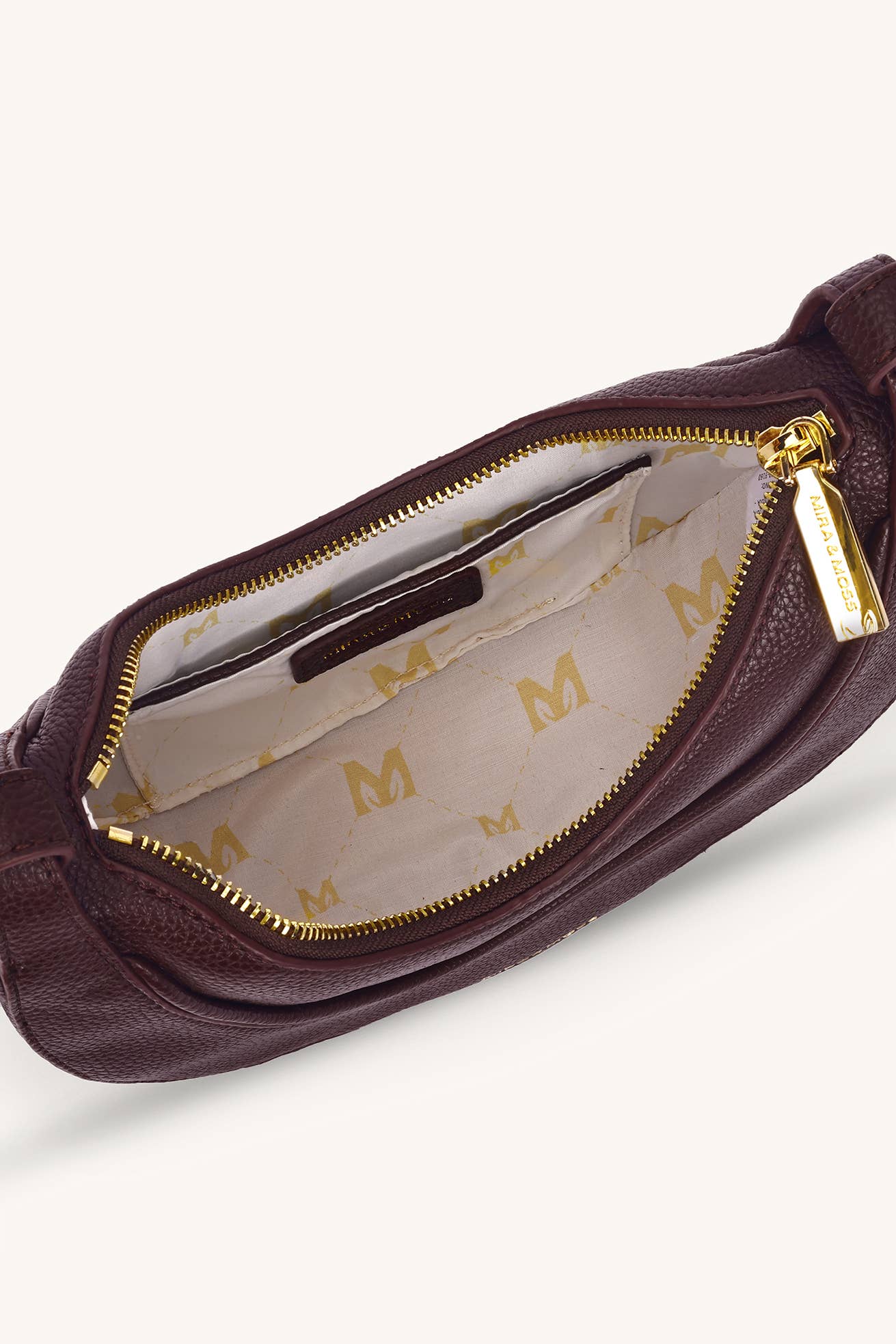 A close-up of a burgundy pebbled leather pouch shown open, revealing a cream-colored interior lined with a repeating gold 'M' pattern and gold-tone zippers.