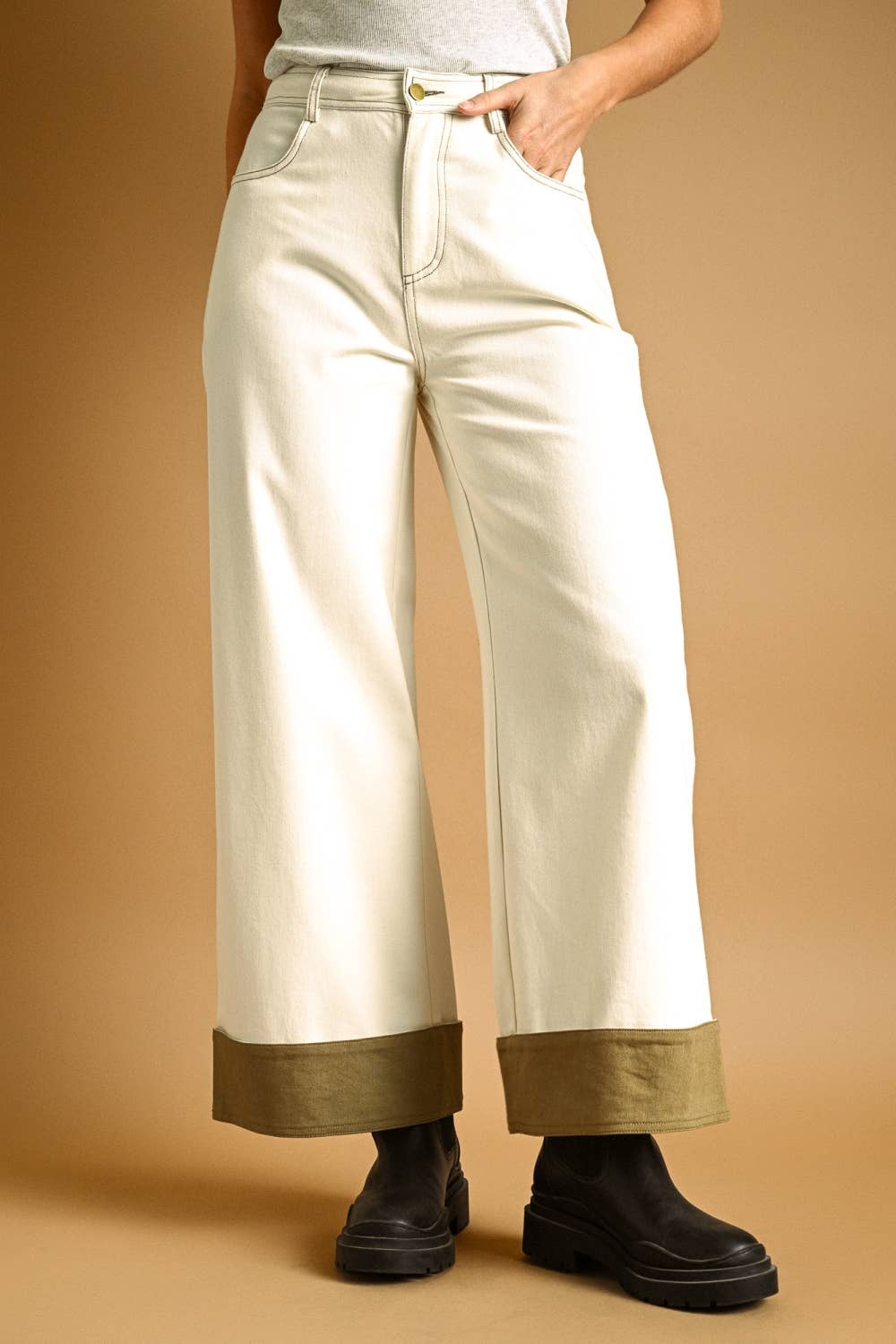 Person wearing cream-colored pants with gold cuffs on a beige background