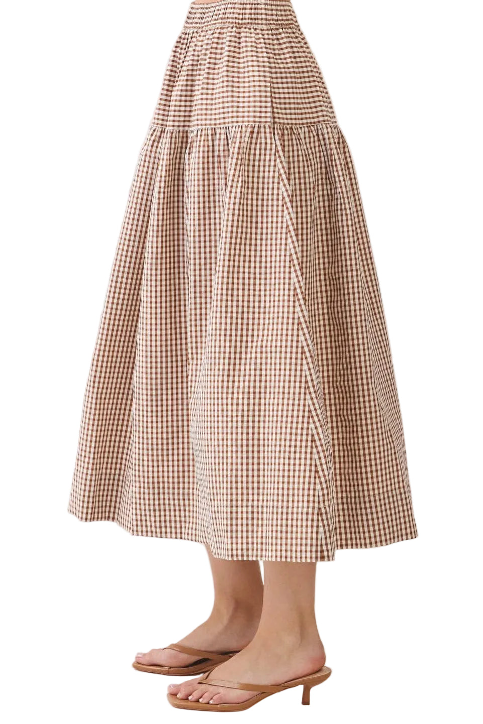 A model wearing a brown and beige gingham tiered midi skirt with flat brown slide sandals, shown from the waist down against a plain light background.