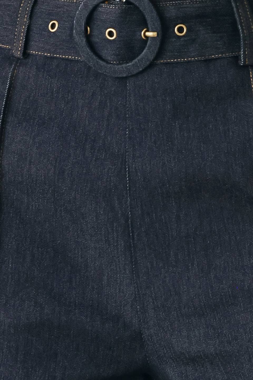 Close-up of dark indigo denim pants showing the waistband with a large circular ring detail and gold-tone metal eyelets.