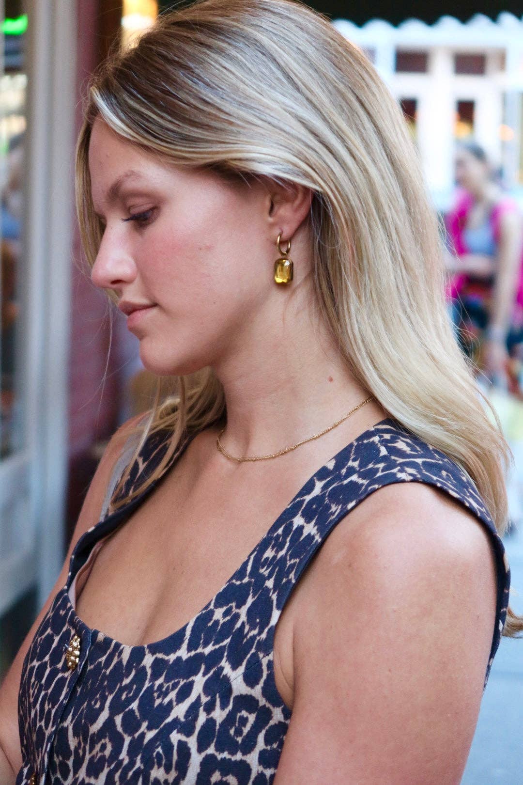 Woman wearing gold earrings and a blue patterned top in an outdoor setting