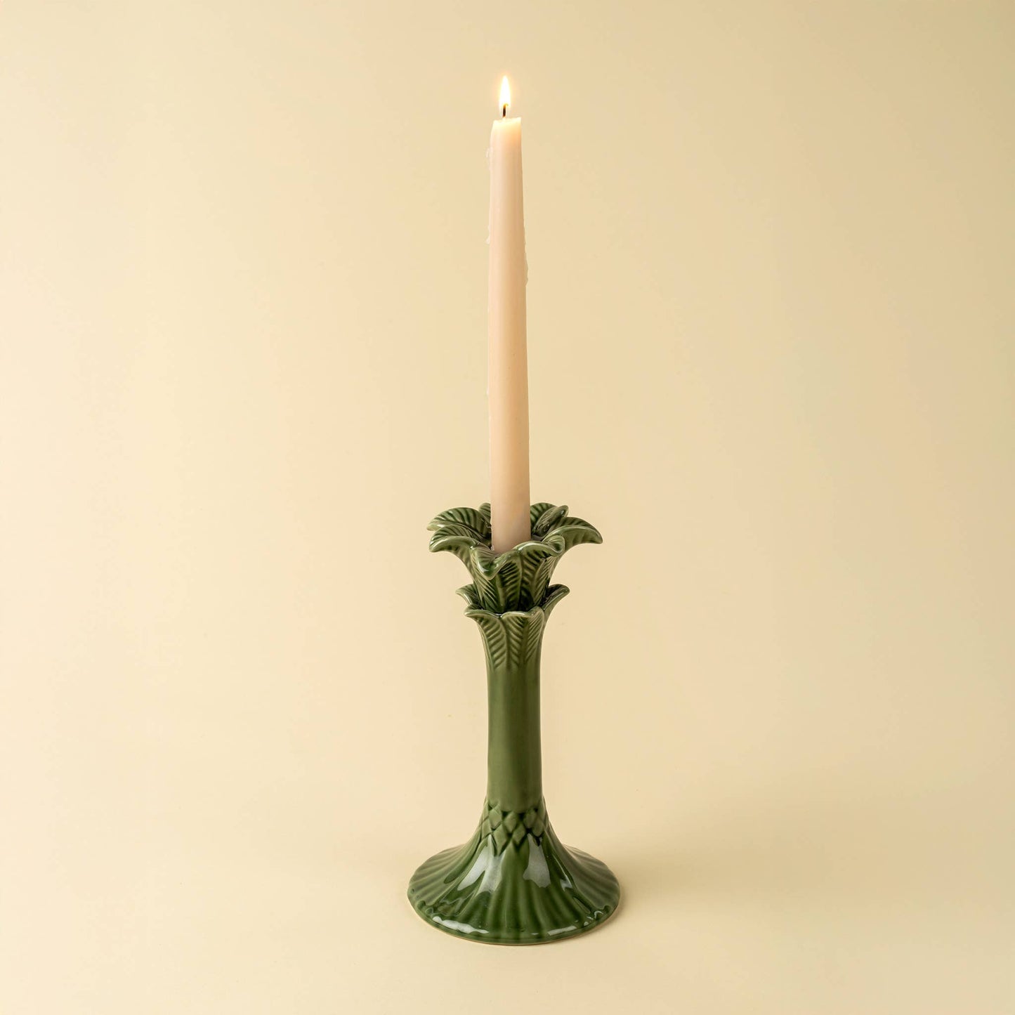 Green candle holder with a lit candle on a beige background