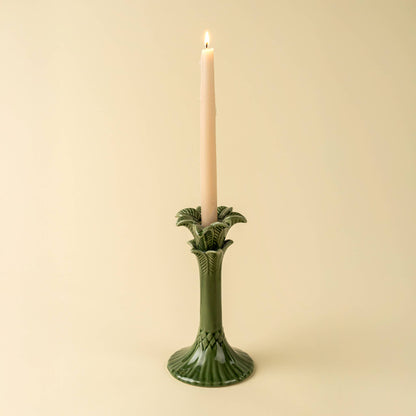 Green candle holder with a lit candle on a beige background