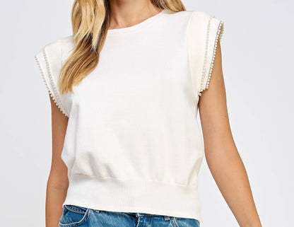 Woman wearing a white sleeveless top with ruffled sleeves and blue jeans on a light gray background