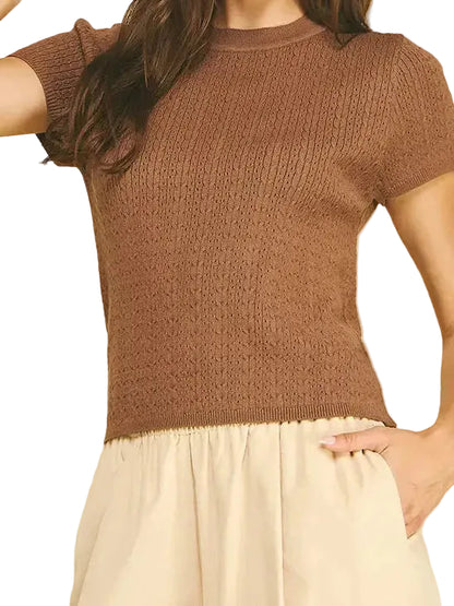 A woman modeling a short-sleeve brown knit top with a crew neck, paired with cream-colored pants, against a solid white background.