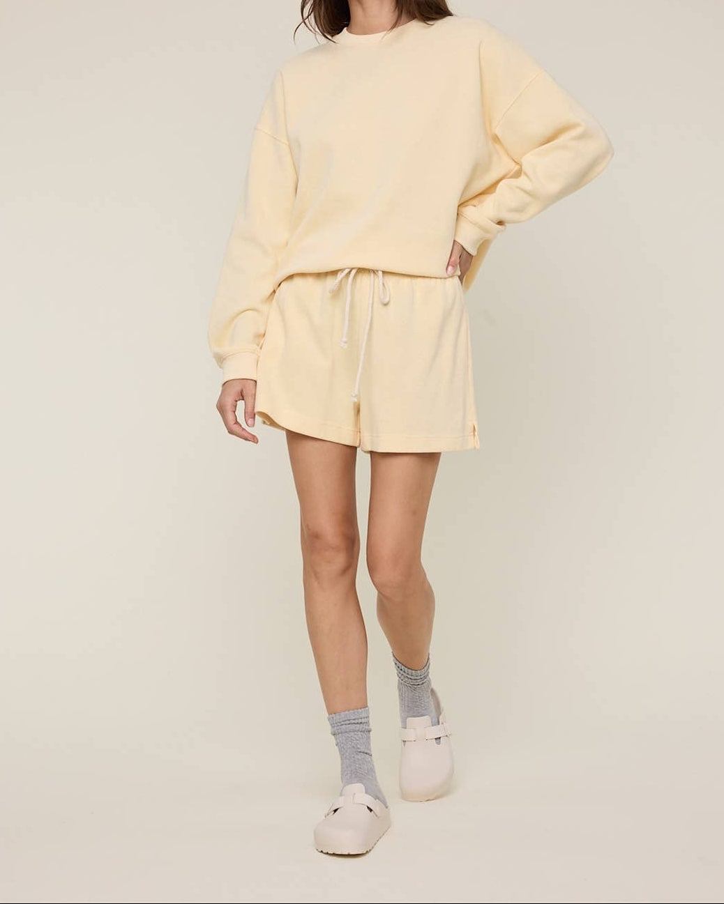 Woman wearing a light yellow outfit with a matching hat on a plain background