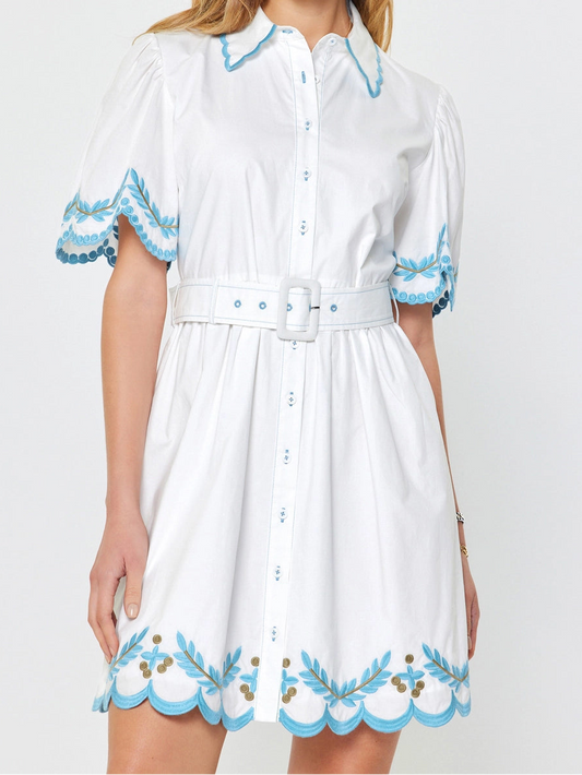 Woman wearing a white dress with blue embroidery on a light gray background