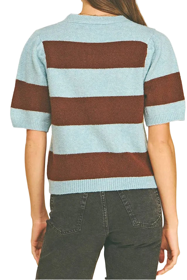 A woman viewed from the back wearing a short-sleeve knit sweater with horizontal light blue and brown stripes, paired with dark gray jeans, against a solid white background.