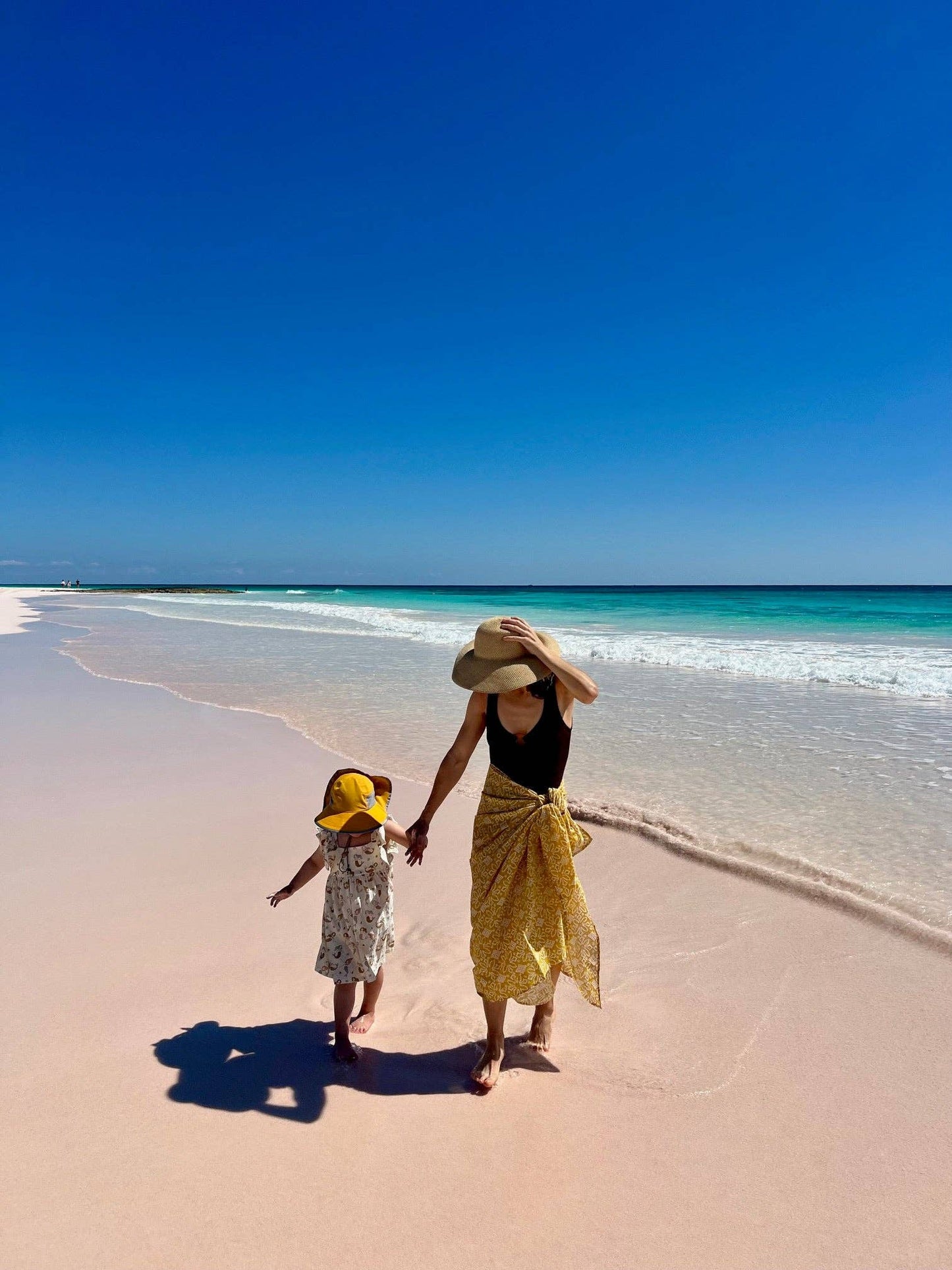 Two people walking on a sandy beach with clear blue sky