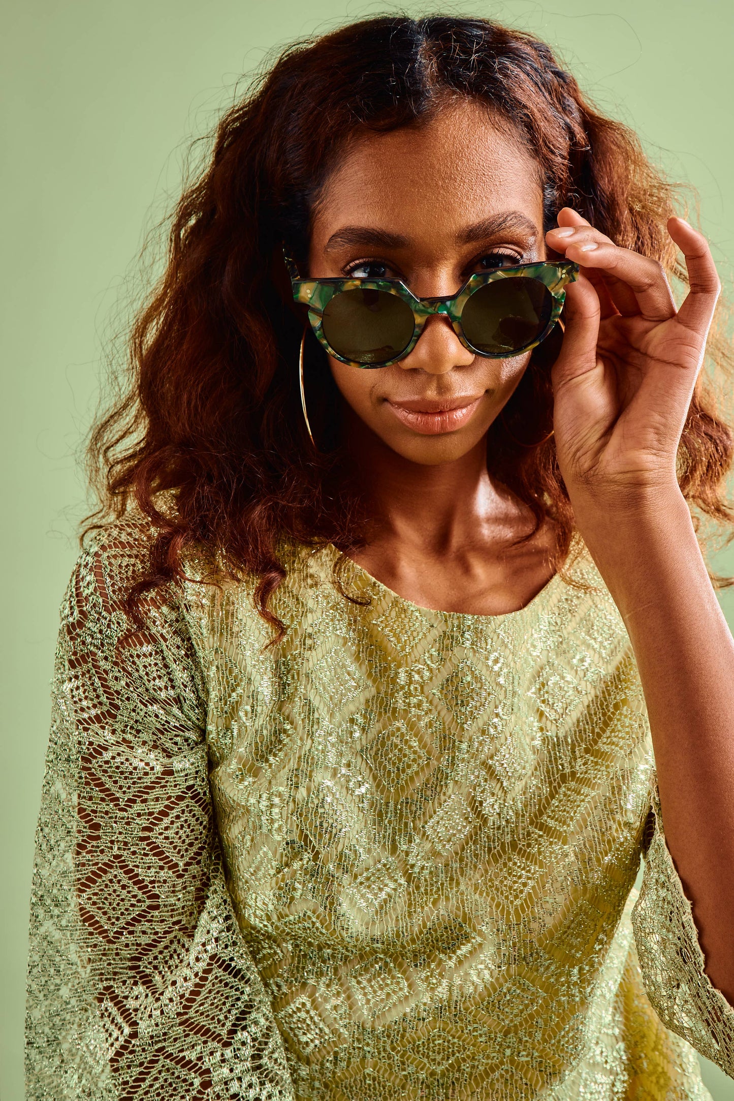 Woman wearing a patterned dress and green sunglasses against a light green background