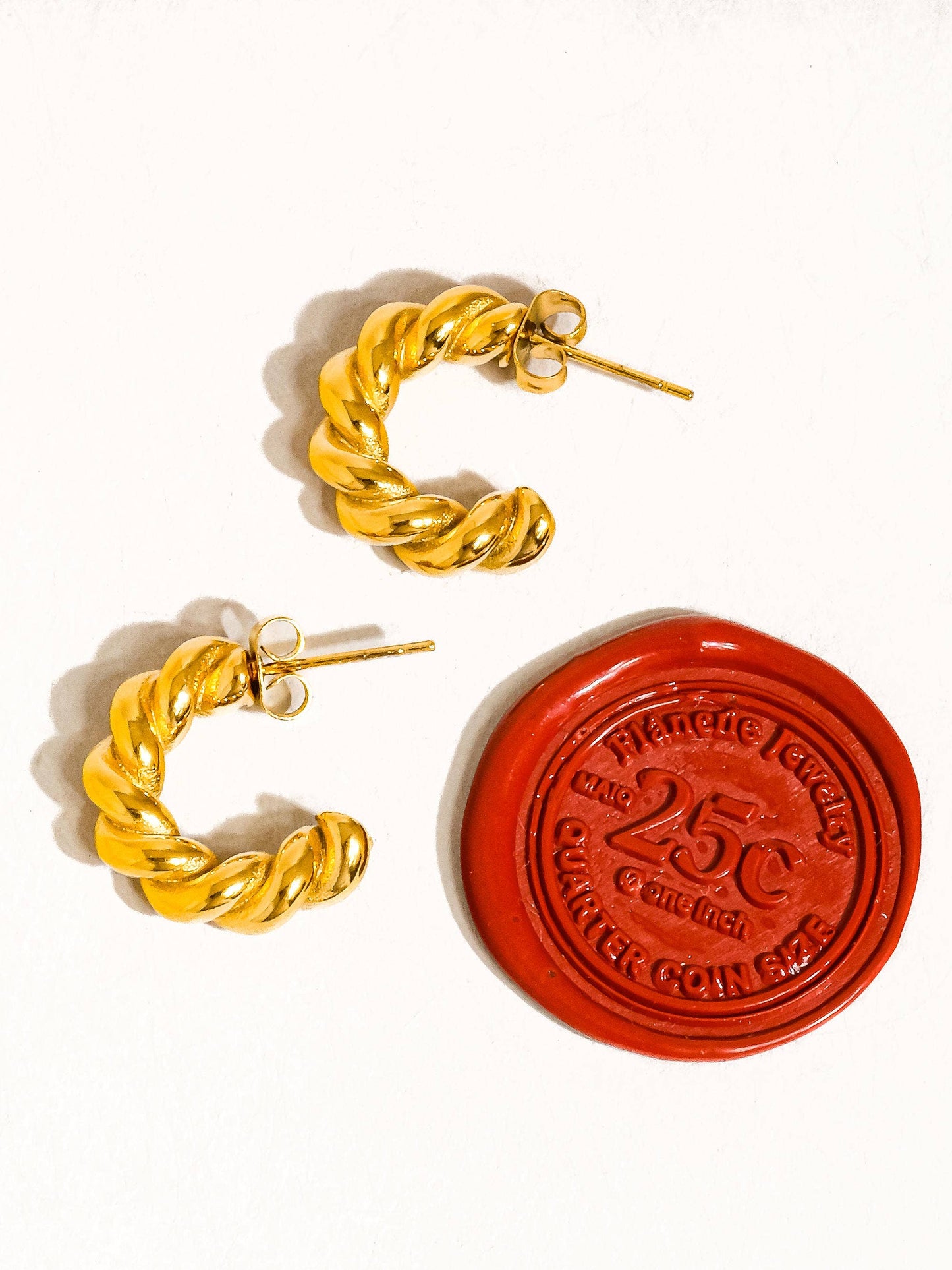 Gold hoop earrings with a red wax seal stamp on a white background